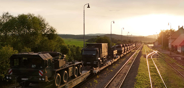 Auf einer Bahnstrecke steht ein Zug aus Flachwagen mit zahlreichen Militärfahrzeugen der Bundeswehr darauf.
