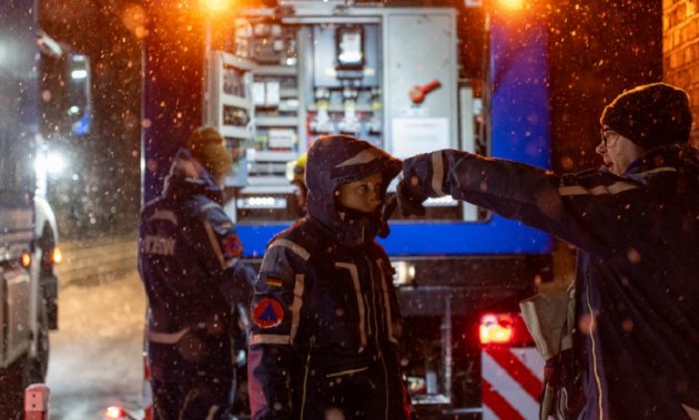 Hinter einem Fahrzeug des Technischen Hilfswerks (THW) stehen mehrere THW-Angehörige im Schneefall; einer von ihnen zeigt in eine Richtung.