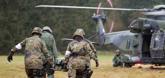 Soldatinnen und Soldaten tragen einen Kameraden zu einem Sanitätshubschrauber