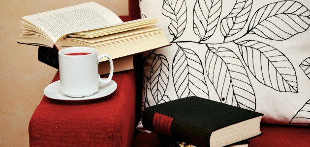 Bücher und eine Tasse Tee auf einem roten Sofa