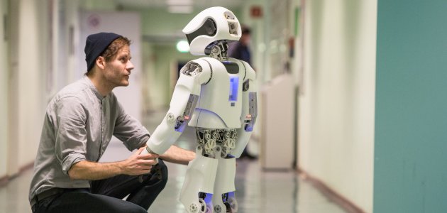 Ein junger Mann hält die Hand eines Roboters und schaut ihm in die Augen.