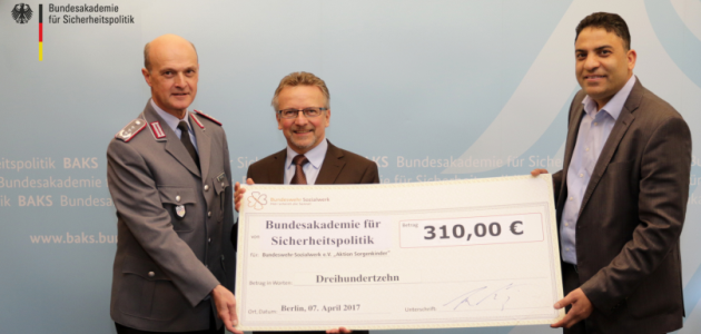 Vor einer blauen Wand mit der Aufschrift BAKS stehen der Direktor Oberst Klaus Hahndel, der Präsident der BAKS Dr. Karl Heinz Kamp und der Betreuungsstellenleiter des Bundeswehr-Sozialwerks Nemer Abou Daher und halten einen übergroßen Spendenscheck.