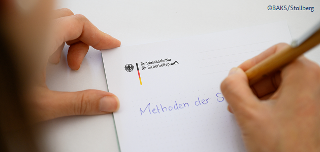 Eine Person schreibt mit einem Kugelschreiber auf einen Notizblock mit Logo der BAKS "Methoden der S..." 