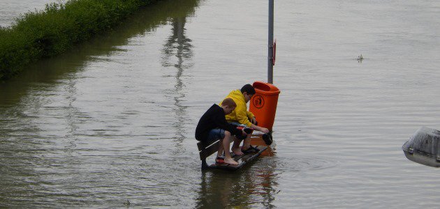 Zwei Kinder sitzen auf einer Bank von Hochwasser umgeben.