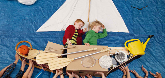 Zwei Jungen sitzen in einem selbstgebauten Boot, werden von vielen Händen getragen.