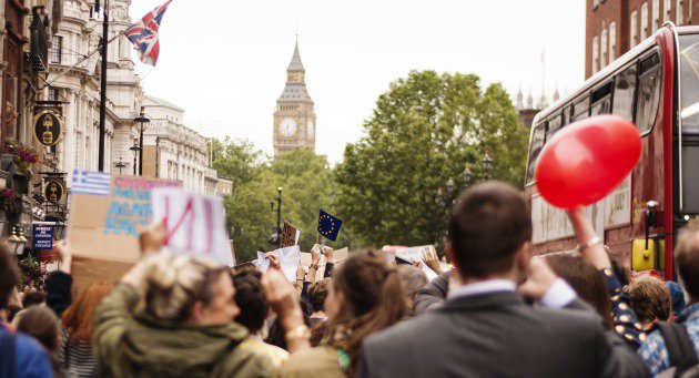 Peope walking on a street, in the background is a big tower with a clock and the union jack.