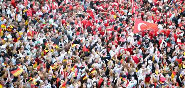 Das Bild zeigt eine beieinander stehende Menschenmenge, deren eine Hälfte als Fans der deutschen Fußball-Nationalmannschaft, die andere als Fans der türkischen Fußball-Nationalmannschaft erkennbar ist.