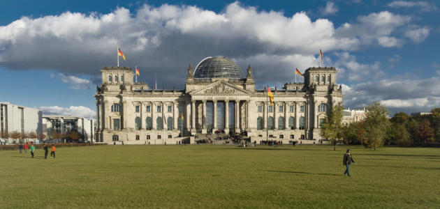 Das Foto zeigt das Plenargebäude des Deutschen Bundestages von Westen; links ist das Paul-Löbe-Haus zu erkennen, rechts Bäume des Großen Tiergartens.