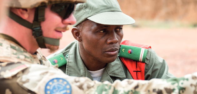 Ein deutscher Soldat zeigt auf etwas; ein nah bei ihm stehender malischer Soldat blickt in diue betreffende Richtung.