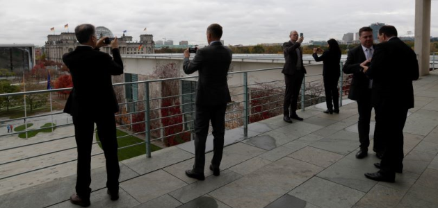Mehrere Menschen stehen Smartphones in der Hand haltend auf der Dachterrasse des Bundeskanzleramts in Berlin und blicken fotografierend zum Reichstag hinüber.