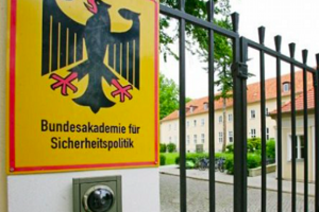 Blick auf ein Schild mit der Aufschrift Bundesakademie für Sicherheitspolitik. Das Schild hängt an einem zaun vor einem Gebäude.