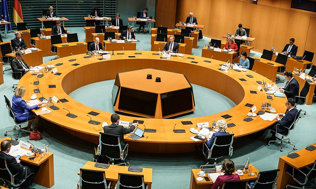 Im Bundeskanzleramt sitzen die Ministerinnen und Minister der Bundesregierung um einen kreisförmigen sowie weitere im Umkreis stehende Tische.
