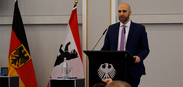 Ahmad Mansour steht sprechend an einem Pult mit dem Bundesadler darauf; links von ihm stehen die Bundesflagge und die Flagge Berlins.