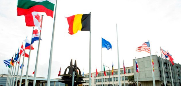Die Flaggen der NATO-Mitgliedsstaaten und der NATO wehen auf dem zentralen Platz im NATO-Hauptquartier in Brüssel; in der Mitte des Platzes steht da NATO-Symbol als metallene Plastik.
