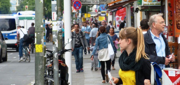 Zahlreiche Menschen stehen und gehen entlang einer Einkaufsstraße in Berlin-Neukölln.