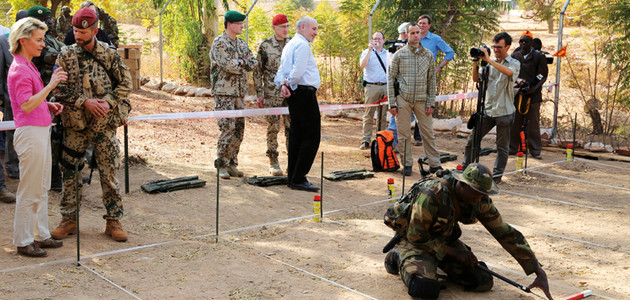 Verteidigungsministerin Ursula von der Leyen besucht die Pionierausbildung des deutschen Einsatzkontingent in Mali; links stehend die Ministerin im Gespräch mit einem deutschen Soldaten, rechts knieend ein malischer Soldat in einem Übungsminenfeld.