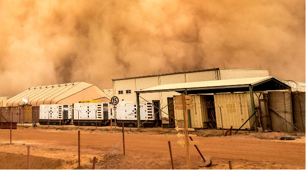 Foto: Bundeswehr/Patrik Bransmöller Hinter den Gebäuden eines militärischen Camps in Mali zieht ein Sandsturm auf, der die gesamte Szenerie in oranges Licht taucht.