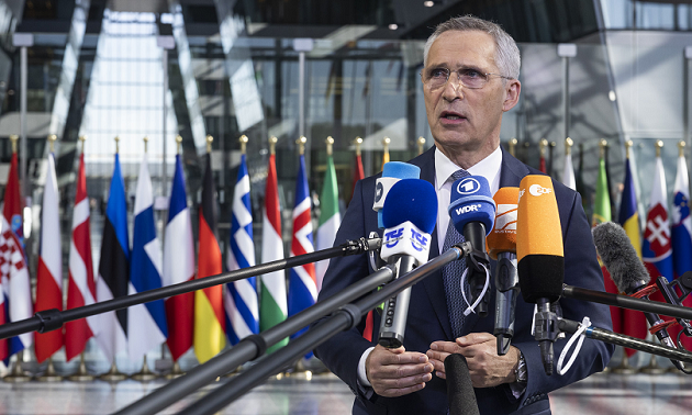 NATO-Generalsekretär steht 2023 in einem Gebäudefoyer vor zahlreichen NATO-Mitgliedsländerflaggen und spricht in viele Mikrofone von Medienhäusern..
