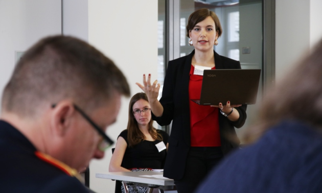 Eine Frau mit einem Notebook in der Hand spricht gestikulierend zu einem uniformierten Offizier.