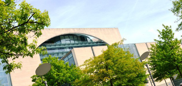 Durch das Laub zweier Bäume ist von schräg unten die Längsfassade des Bundeskanzleramts in Berlin zu sehen.