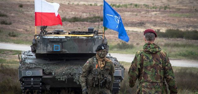 Ein Kampfpanzer mit NATO- und polnischer Flagge sowie zwei Soldaten auf einem militärischen Übungsgelände in Polen