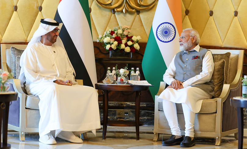 Indian Prime Minister Modi and COP 28 President-elect and Abu Dhabi National Oil Company CEO Al Jaber sit in front of their state flags and chat.