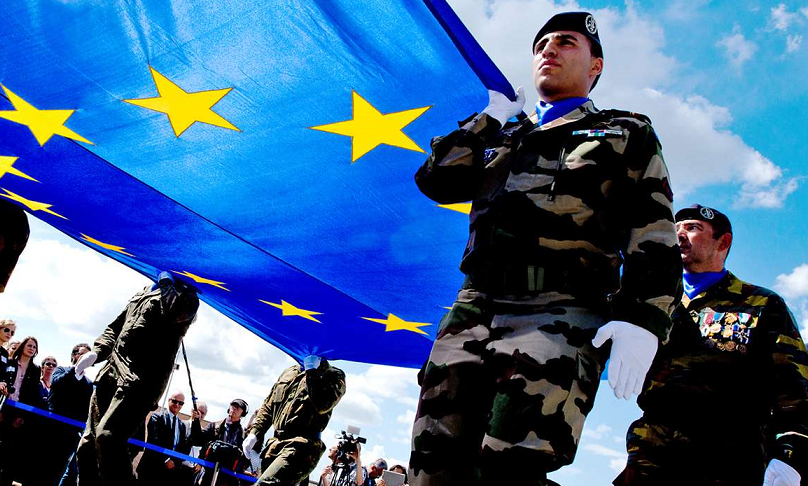 Soldaten unterschiedlicher Nationen halten eine große EU Fahne hoch