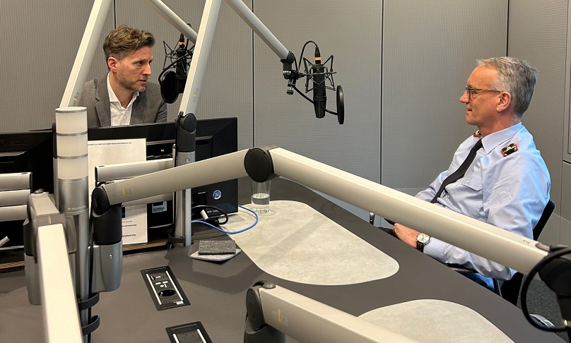 Der Hörfunkmoderator Uli Hauck und BAKS-Präsident Generalmajor Stahl sitzen in einem Studio mit Mikrofonen.