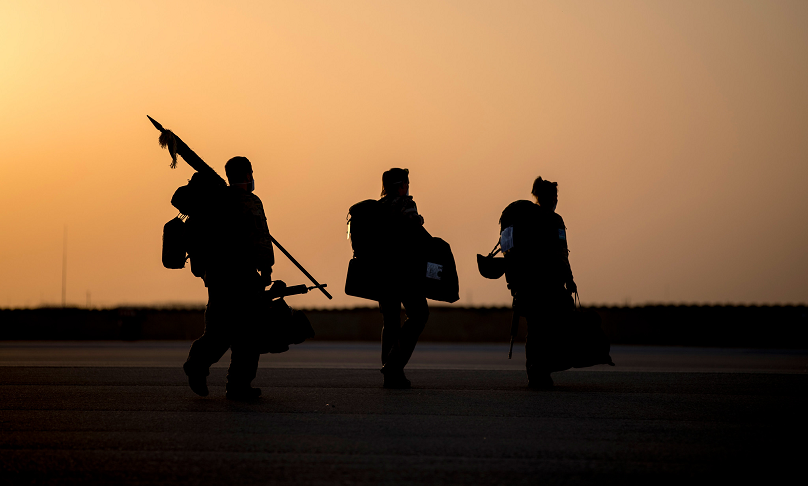Drei Bundeswehrsoldatinnen und -soldaten laufen mit militärischer Ausrüstung am Körper vor einem Sonnenuntergang durchs Bild.