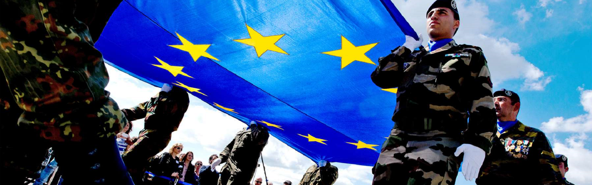 Soldaten unterschiedlicher Nationen halten eine große EU Fahne hoch